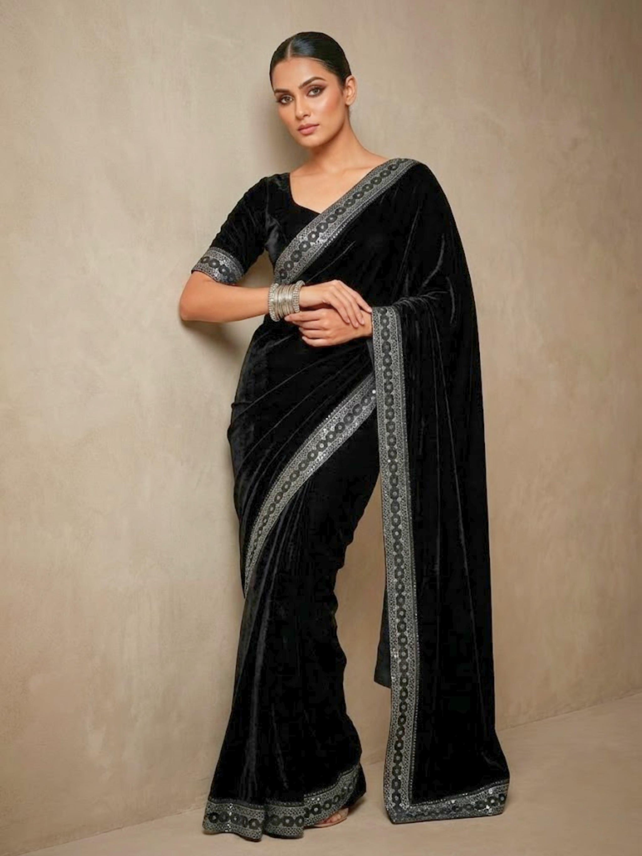 Woman wearing a black saree with silver border against a beige background