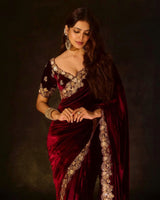 Woman wearing a maroon saree with gold embroidery against a dark background