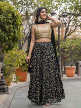 Woman in a black and gold traditional outfit standing outdoors with greenery in the background
