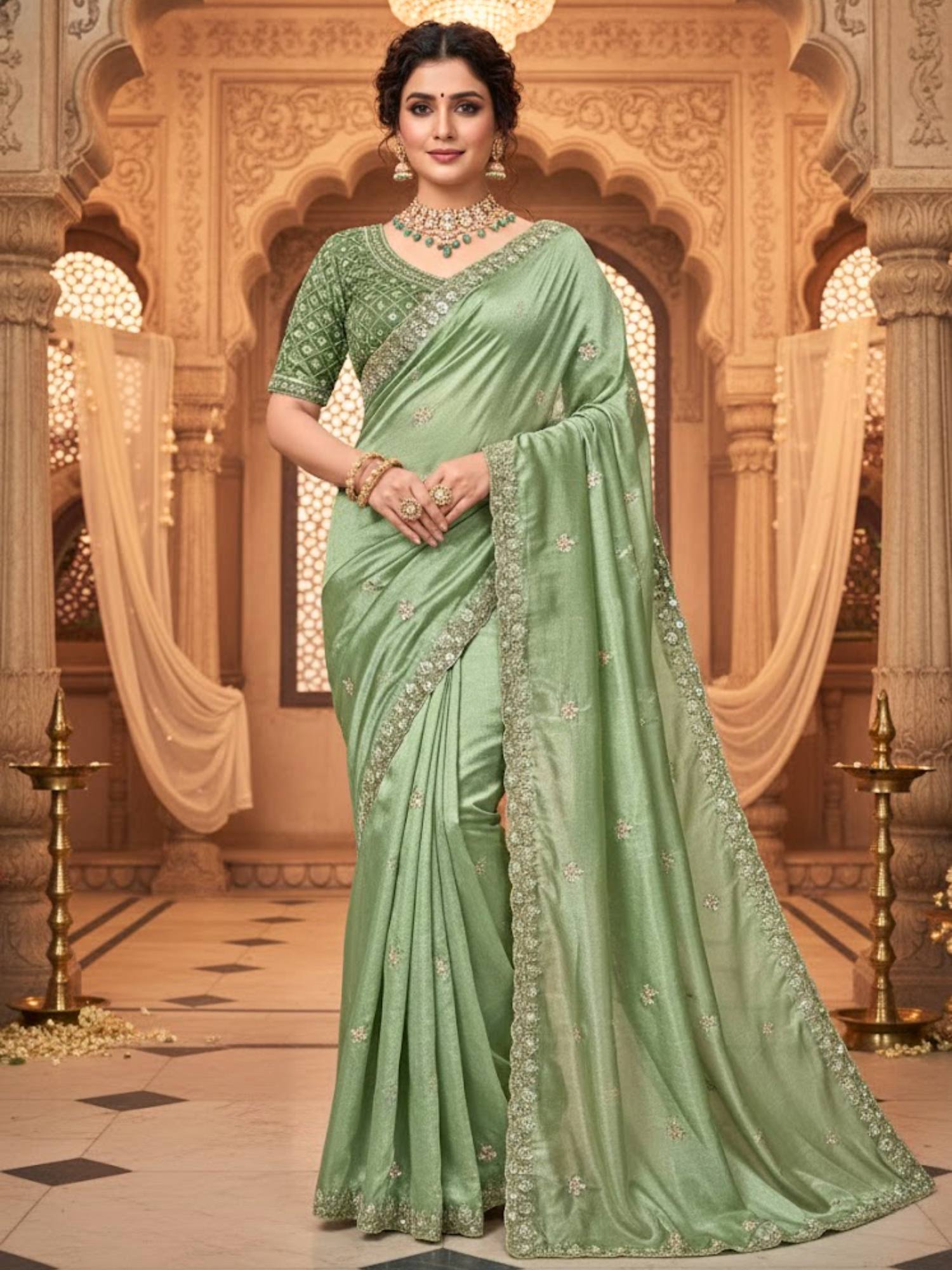 Woman in a light green saree with intricate patterns standing in an ornate indoor setting.