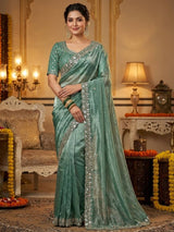 Woman in a light blue saree with silver border in an elegant room.